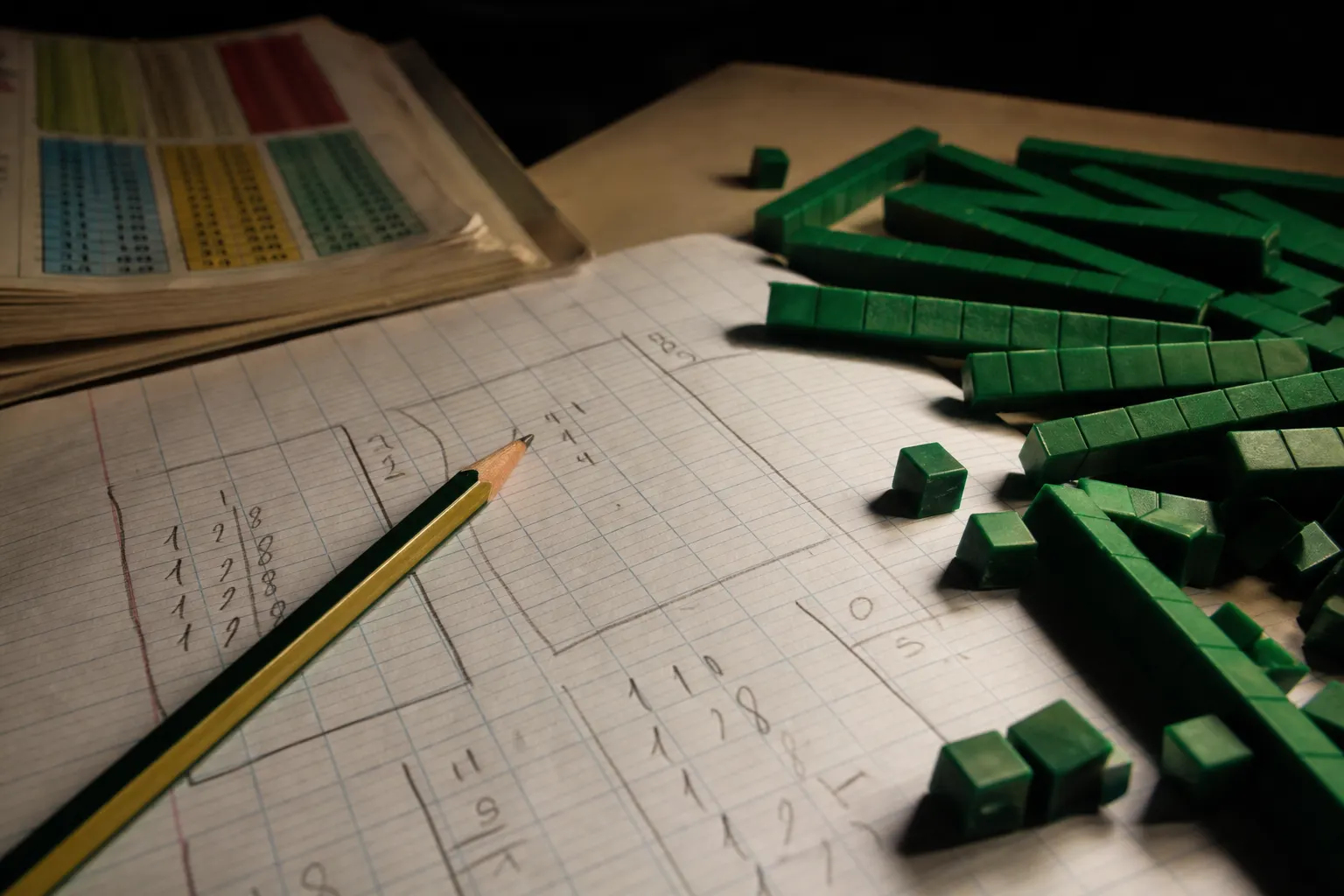Une fiche de division posée avec un crayon, une table de multiplication et des cubes de numération.
