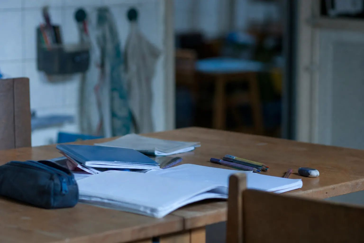Un enfant de CM1 travaille calmement à une table avec un cahier, des crayons et des livres scolaires.
