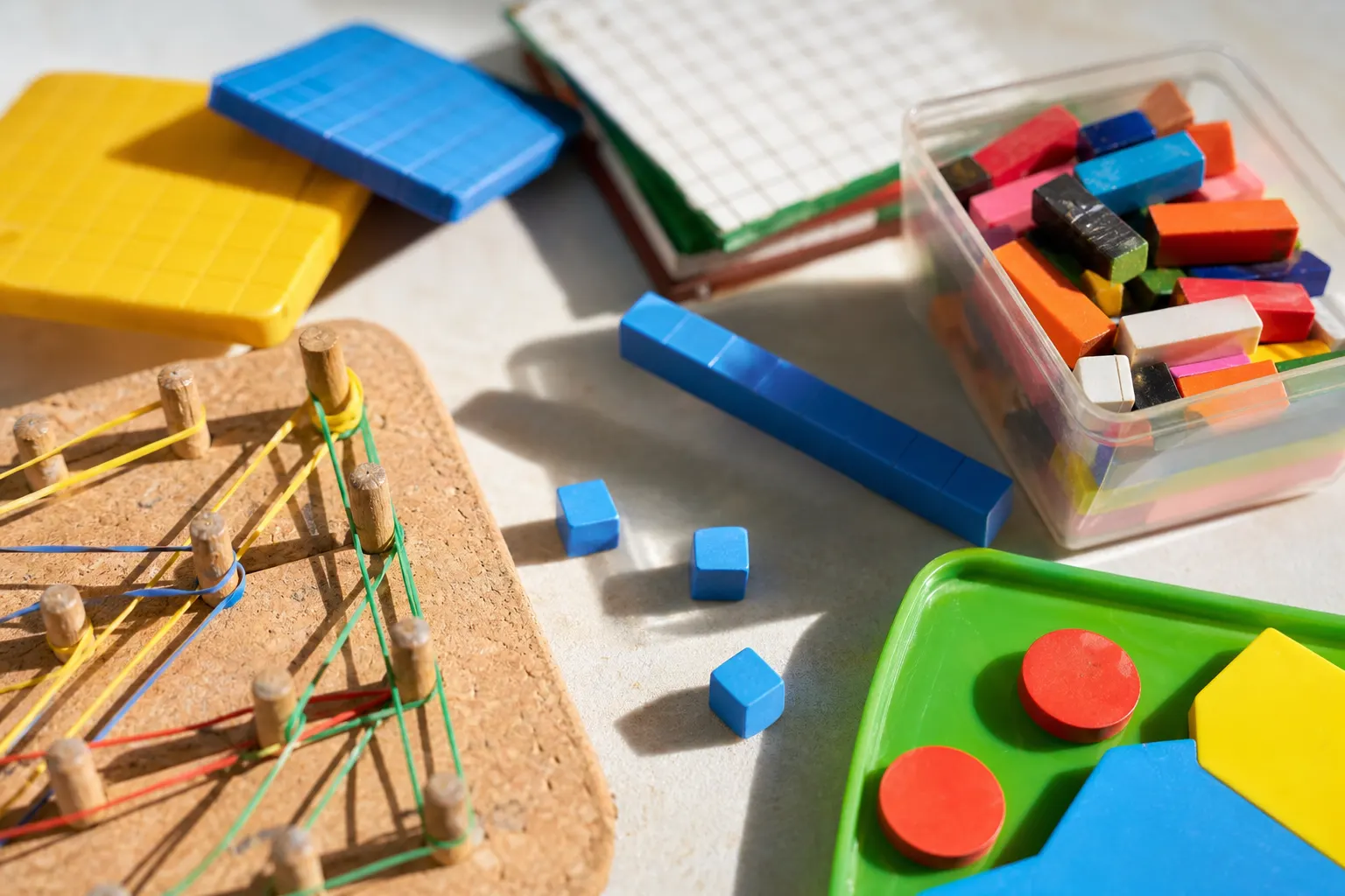 Un enfant de CE1 travaille à une table avec des cubes de comptage, une règle, un cahier et des crayons.